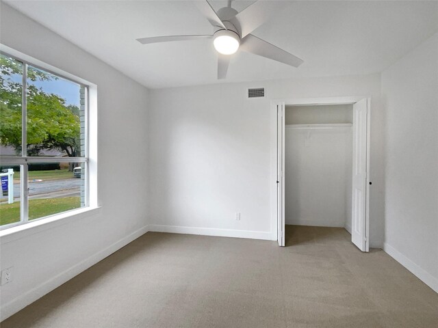 unfurnished bedroom with light carpet, a closet, multiple windows, and ceiling fan