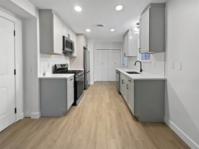 kitchen featuring stainless steel appliances, sink, gray cabinetry, and light hardwood / wood-style flooring