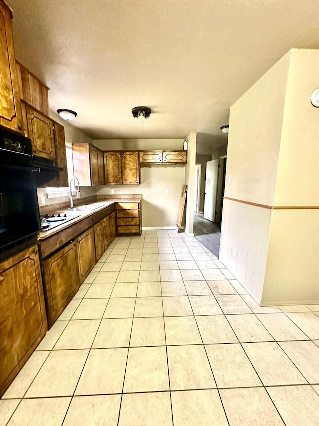 kitchen featuring white gas stovetop, sink, light tile patterned floors, a textured ceiling, and black oven