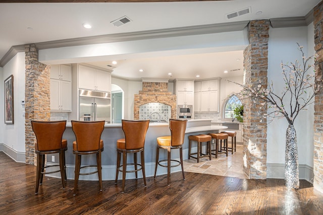 kitchen featuring white cabinetry, a breakfast bar, built in appliances, and crown molding