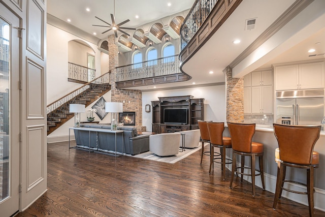 living room with ceiling fan, a fireplace, dark hardwood / wood-style flooring, and a high ceiling