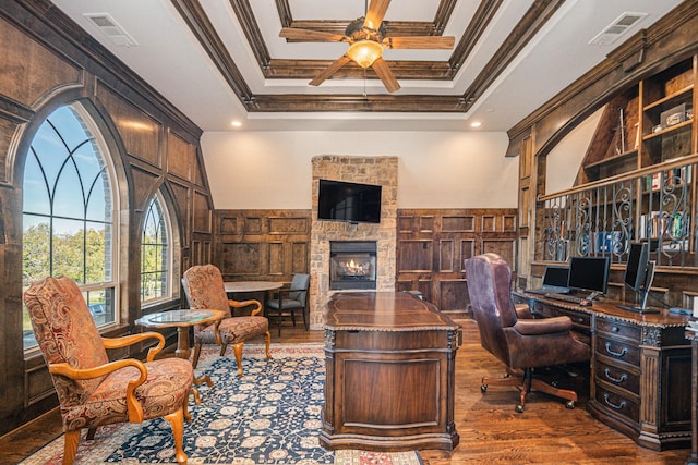 office space featuring crown molding, a stone fireplace, dark hardwood / wood-style floors, and ceiling fan