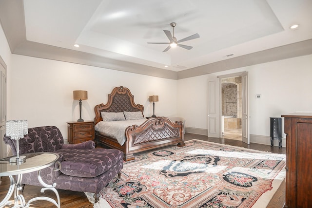 bedroom with hardwood / wood-style flooring, ceiling fan, ensuite bathroom, and a tray ceiling