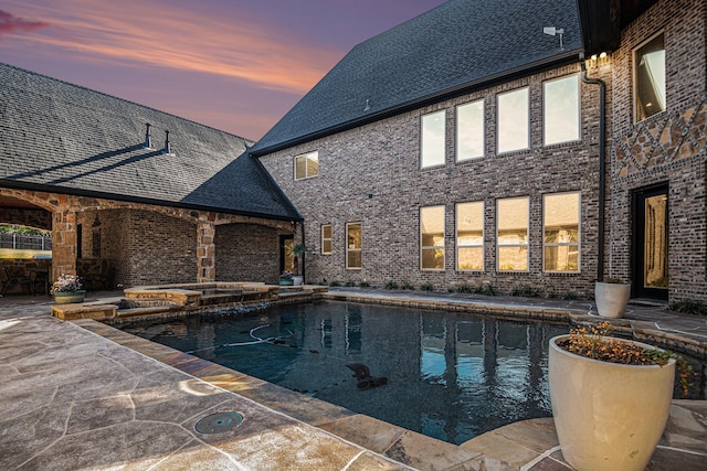 pool at dusk with a patio and an in ground hot tub