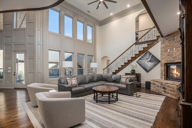 living room with hardwood / wood-style floors, a stone fireplace, ceiling fan, and a towering ceiling