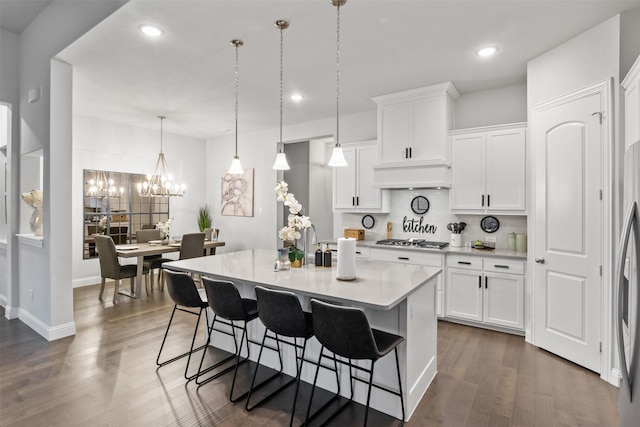 kitchen with stainless steel gas stovetop, a kitchen island with sink, dark hardwood / wood-style floors, decorative light fixtures, and white cabinetry