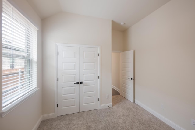 unfurnished bedroom with light carpet, a closet, multiple windows, and lofted ceiling