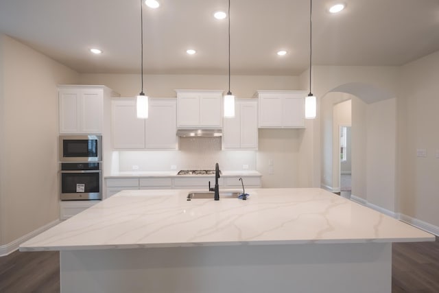 kitchen with light stone countertops, pendant lighting, stainless steel appliances, and a center island with sink