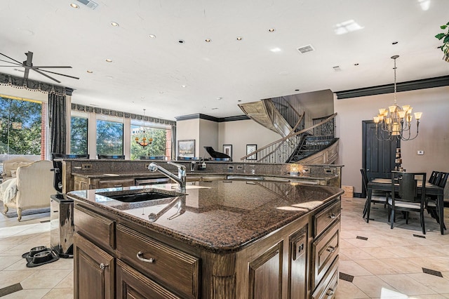 kitchen featuring sink, dark stone counters, light tile patterned floors, a center island with sink, and an inviting chandelier