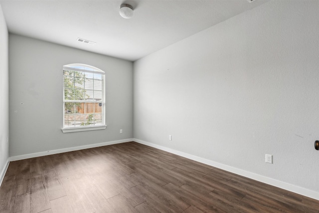 spare room with dark wood finished floors, visible vents, and baseboards