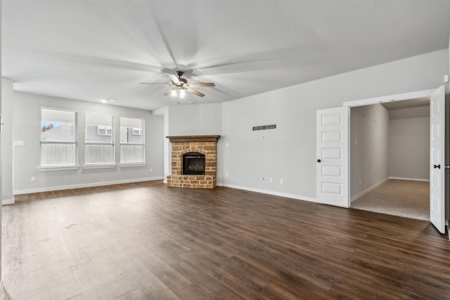 unfurnished living room featuring dark wood-type flooring, a fireplace with raised hearth, baseboards, and ceiling fan