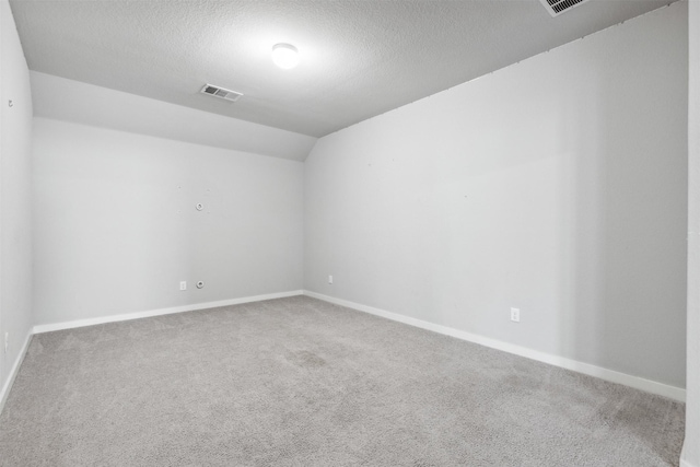 carpeted empty room with visible vents, a textured ceiling, baseboards, and vaulted ceiling