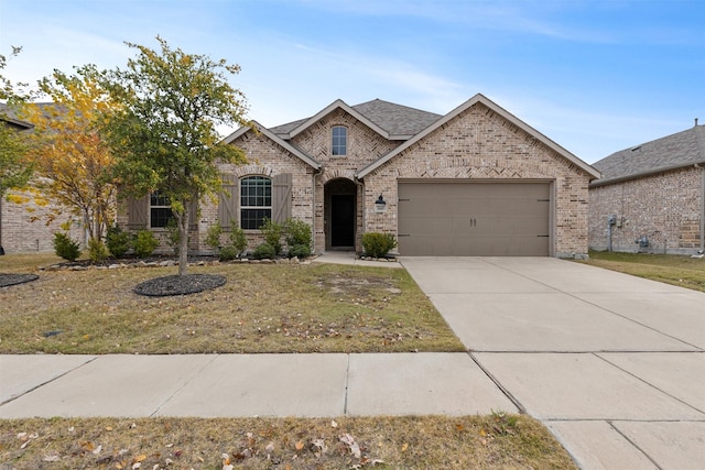 french country style house featuring brick siding, an attached garage, a front lawn, roof with shingles, and driveway