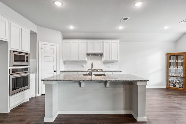 kitchen with light stone counters, dark wood-style floors, a sink, stainless steel appliances, and under cabinet range hood