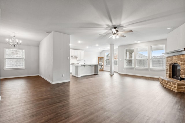unfurnished living room featuring ceiling fan with notable chandelier, dark wood-type flooring, a fireplace, and baseboards