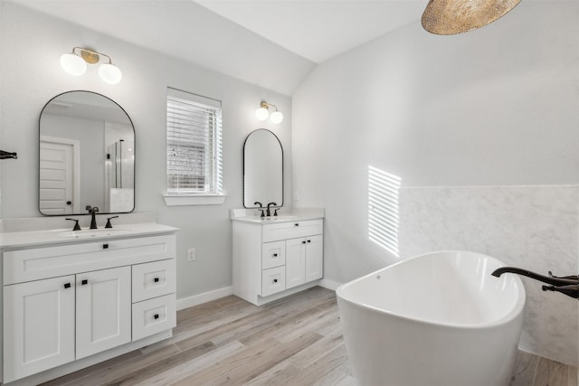 full bath featuring a soaking tub, two vanities, wood finished floors, and a sink