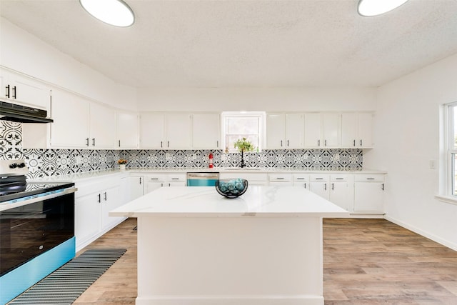 kitchen with backsplash, stainless steel appliances, white cabinets, a kitchen island, and light wood-type flooring