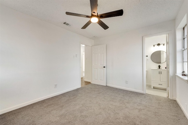 unfurnished bedroom with ensuite bathroom, sink, light colored carpet, ceiling fan, and a textured ceiling