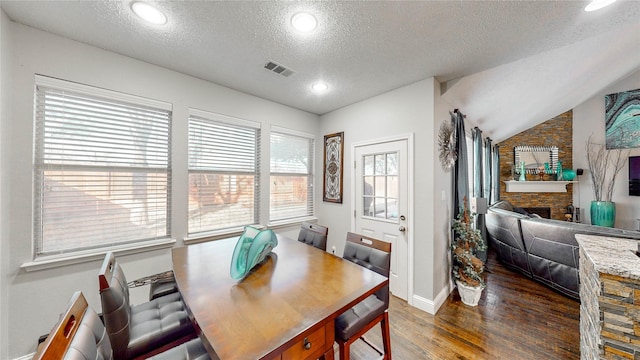 dining area featuring a stone fireplace, lofted ceiling, dark wood-type flooring, and a textured ceiling