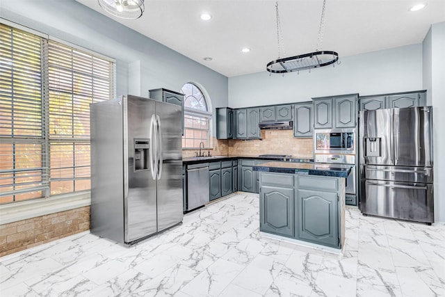 kitchen with sink, hanging light fixtures, tasteful backsplash, a kitchen island, and appliances with stainless steel finishes