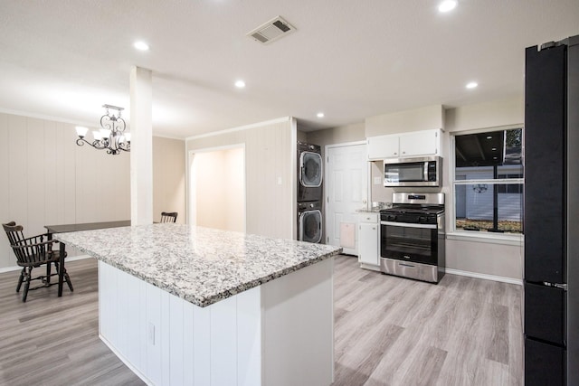 kitchen with stainless steel appliances, stacked washing maching and dryer, white cabinets, and light wood-type flooring