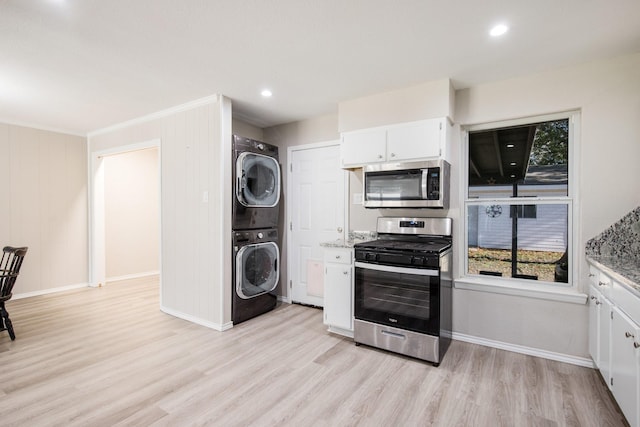 kitchen featuring appliances with stainless steel finishes, white cabinetry, stacked washer and clothes dryer, light stone counters, and light wood-type flooring