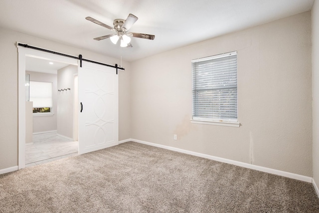 unfurnished bedroom featuring multiple windows, a barn door, ceiling fan, and carpet flooring