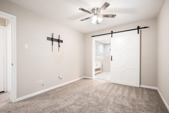 unfurnished bedroom with ceiling fan, a barn door, carpet flooring, and ensuite bath