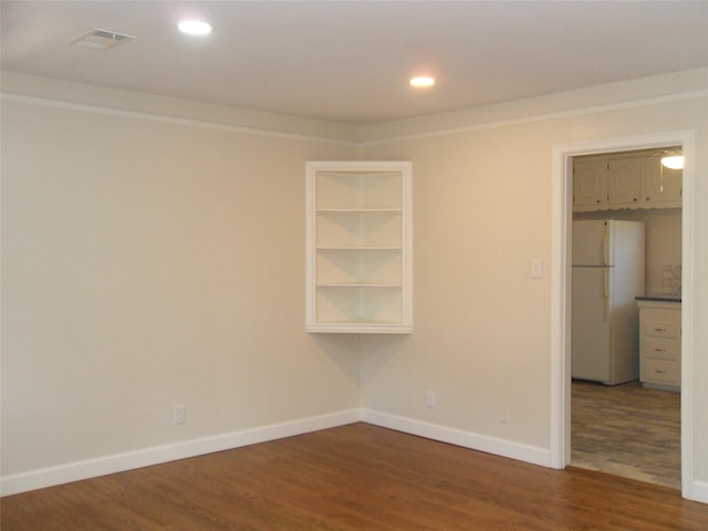 spare room with wood-type flooring, crown molding, and built in shelves