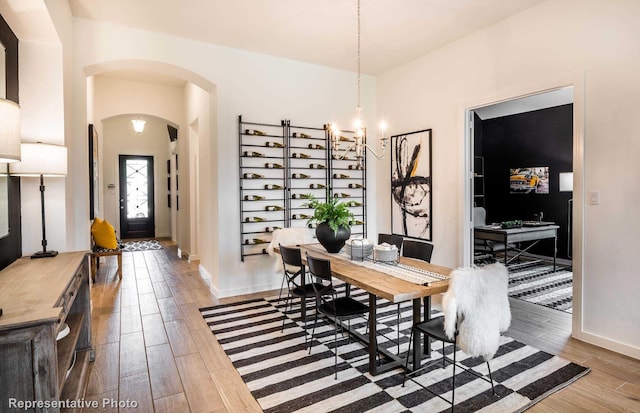 dining room featuring a notable chandelier, wood finished floors, arched walkways, and baseboards