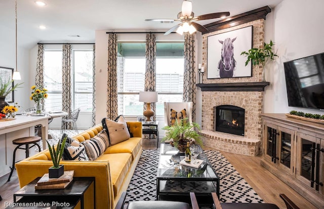 living room with a wealth of natural light, a fireplace, ceiling fan, and wood finished floors