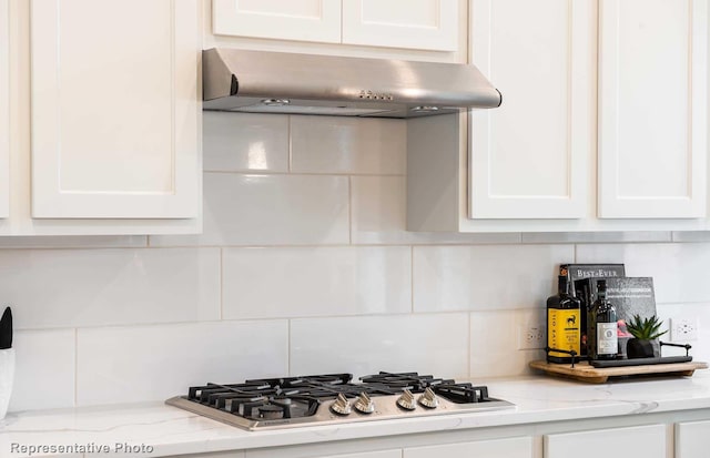 kitchen featuring light stone countertops, stainless steel gas cooktop, decorative backsplash, white cabinets, and under cabinet range hood