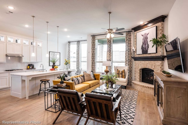 living room featuring a ceiling fan, visible vents, light wood-style flooring, recessed lighting, and a fireplace