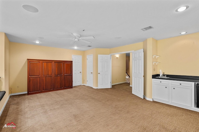 unfurnished living room with ceiling fan, sink, and light carpet