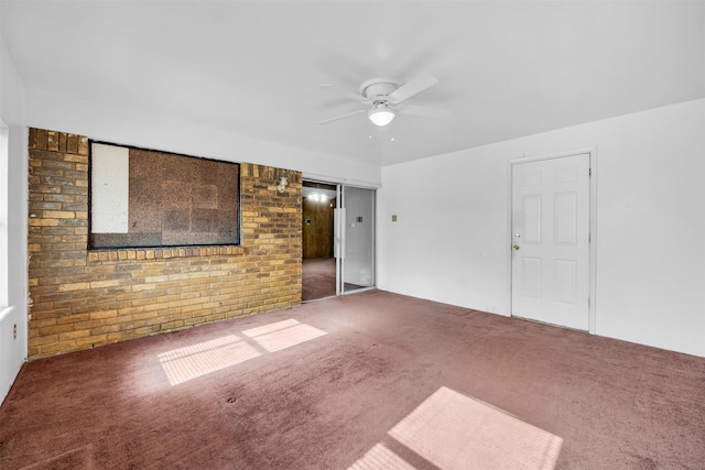 empty room featuring dark colored carpet, ceiling fan, and brick wall