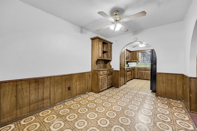 home office with ceiling fan, a textured ceiling, and wooden walls