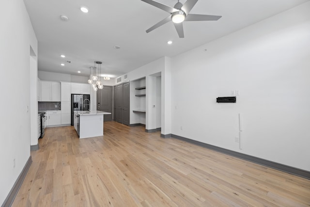 kitchen featuring hanging light fixtures, a center island with sink, light hardwood / wood-style floors, decorative backsplash, and white cabinets