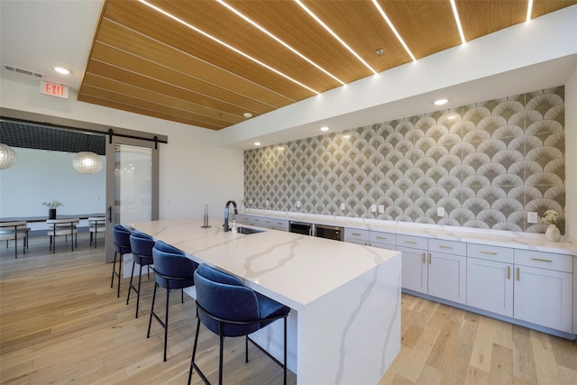 kitchen featuring a breakfast bar, wood ceiling, light stone counters, a center island with sink, and a barn door