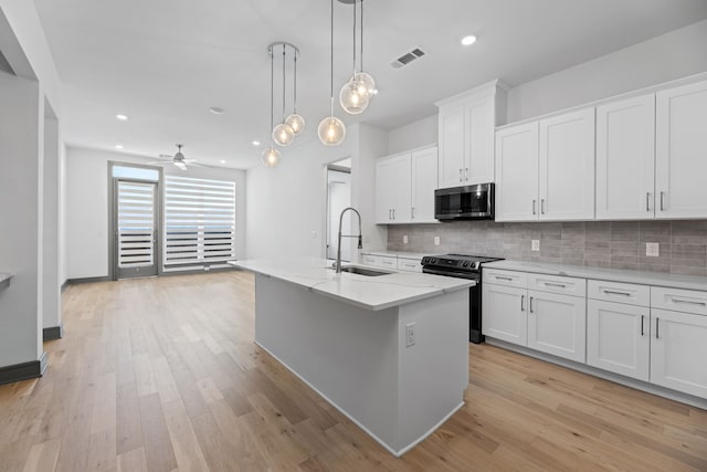 kitchen featuring pendant lighting, sink, a kitchen island with sink, white cabinets, and black / electric stove