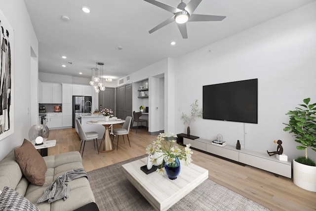 living room with ceiling fan with notable chandelier and light hardwood / wood-style floors