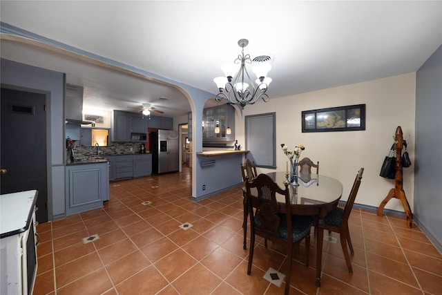 tiled dining space featuring sink and ceiling fan with notable chandelier