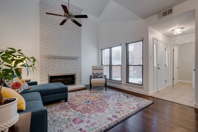 living room with hardwood / wood-style floors, ceiling fan, high vaulted ceiling, and a brick fireplace