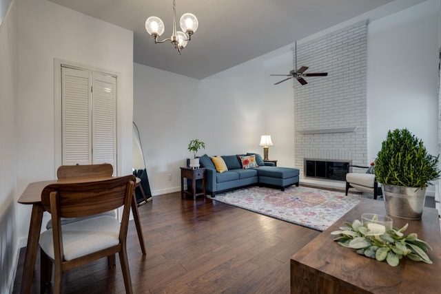 living room with dark hardwood / wood-style floors, ceiling fan with notable chandelier, and a brick fireplace