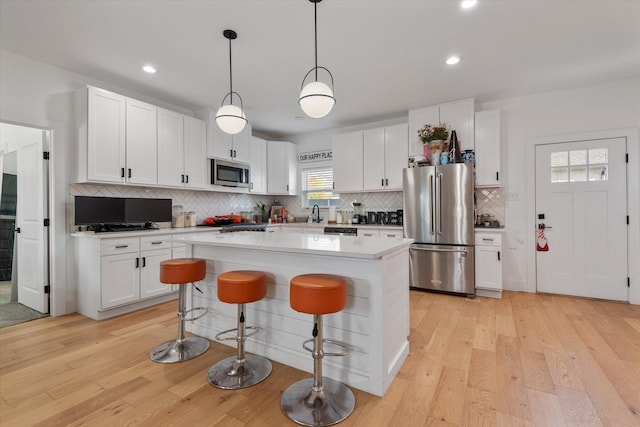 kitchen featuring white cabinetry, a center island, light hardwood / wood-style flooring, pendant lighting, and stainless steel appliances