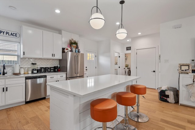 kitchen featuring pendant lighting, appliances with stainless steel finishes, washer and dryer, white cabinets, and a kitchen island