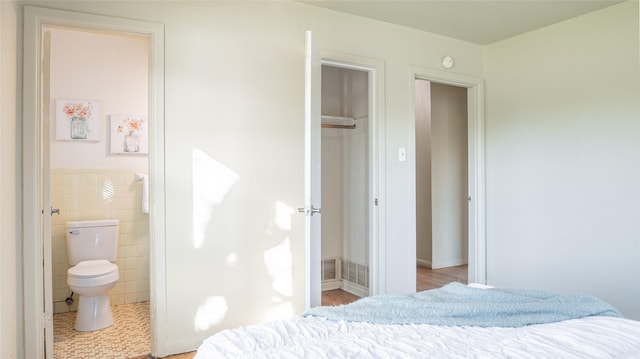 tiled bedroom featuring ensuite bathroom, a closet, and tile walls