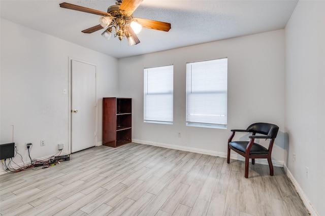 living area featuring ceiling fan, light hardwood / wood-style floors, and a textured ceiling