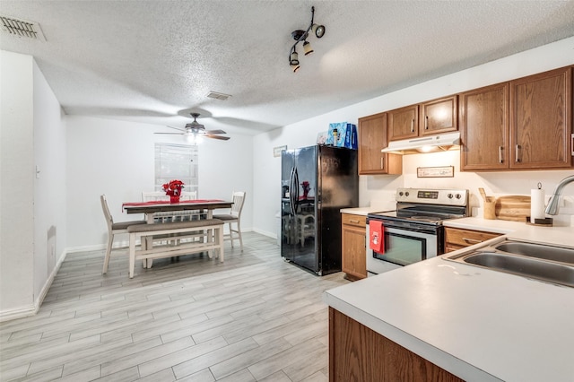 kitchen with stainless steel electric range oven, sink, black fridge, a textured ceiling, and light wood-type flooring