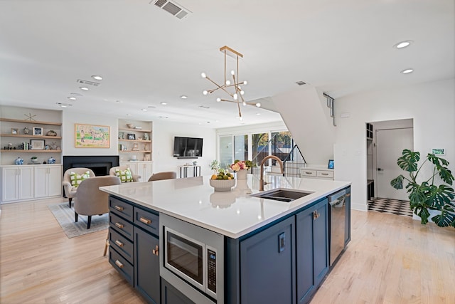 kitchen with sink, appliances with stainless steel finishes, a kitchen island with sink, pendant lighting, and light hardwood / wood-style floors