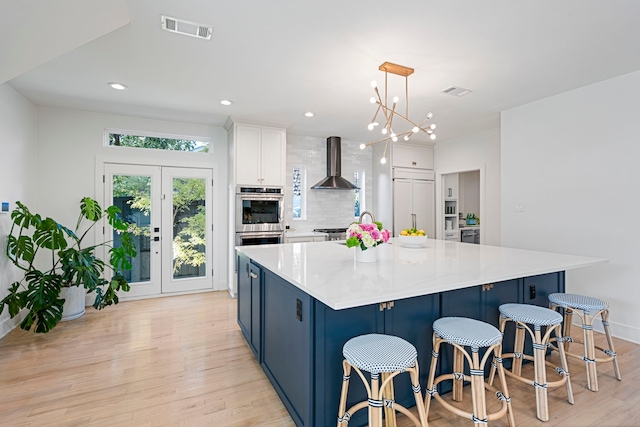 kitchen with a spacious island, paneled fridge, pendant lighting, wall chimney range hood, and white cabinets